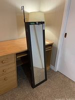Full view of the closed jewelry cabinet leaning against a desk, mirror on front surface