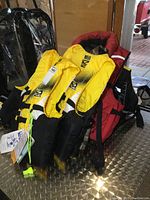 Four yellow Fluid adult life jackets with some new with tags, one maroon inflatable vest behind them.