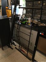 Full view of black metal bed frame components positioned upright against a cabinet, showing headboard and side rails.