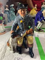 Front view of Royal Doulton The Huntsman HN 2492 figurine showing seated male hunter with dog.