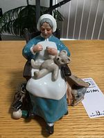 Front view of the Royal Doulton figurine showing elderly woman sewing with teddy bear on lap and small doll beside chair.