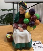 Front view of Royal Doulton figurine, showing elderly woman holding multicolored balloons and seated next to a basket.