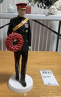 Front view of Royal Doulton figurine of Prince Henry of Wales holding a red poppy wreath, standing on a white base.