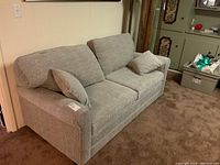 Full view of gray upholstered pull-out sofa with two matching throw pillows, showing style and overall condition.