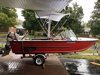 Side view of red boat on white-painted single axle trailer under canopy.