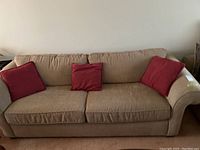 Frontal view of beige sofa with three red pillows on carpeted floor