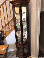 Wood curio cabinet with glass shelves displaying figurines, three-sided glass and mirrored back, stairs in background