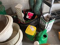 Plastic garden items grouped on garage floor including cream-colored plastic planters, green watering can, and Miracle-Gro container