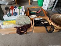Photo showing all items in the lot: glass watering bulbs in styrofoam tray, wooden basket with hose and connector, wooden tray with metal liner and garden tools, and wooden box with accessories.