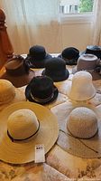 Photo showing 11 assorted ladies hats including straw, felt, and fabric varieties spread over a bed with window background.