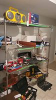Metal wire shelf rack with various tools and household items placed on the shelves for display only. Rack is in basement with neutral colored walls and tiled floor.
