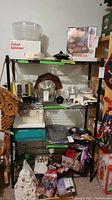 Photo shows black metal wire shelf rack with kitchen and miscellaneous items on shelves for context. The shelving is open wire grid design with scalloped edges.