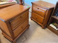 Pair of light brown wooden night tables standing on carpeted floor, showing their front and side views.