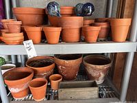 Photo showing terracotta pots from small to large sizes arranged on metal shelving along with glass watering bulbs placed inside some pots.