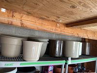 Eight plastic planters on metal shelves, beige, white and dark brown, weathered condition.