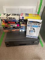 Sharp VC-H976 VHS player with VHS tapes stacked beside it and a radio flyer atop the VHS player.