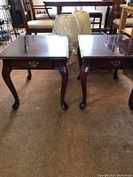Two wood side tables with cabriole legs, dark finish, and slide-out drawers with brass handles visible from front view.