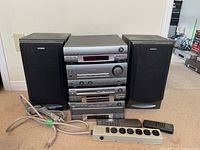 Sony stereo mini hi-fi components stacked with two black Sony speakers on sides, including power and extension cords and two remotes in front.
