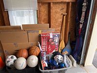 Wide view of sports balls, paddles, exercise bands, fishing rod and other assorted sports equipment in bins and cardboard boxes