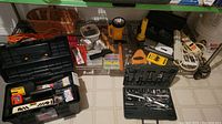 Overview of tools and hardware including cordless drill, flashlight, toolbox and assorted items on floor under shelf.