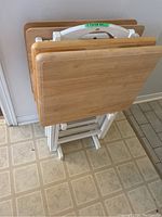 Three wooden TV trays with light wood tops and white folding legs leaning in white wooden caddy, showing how they are stored.