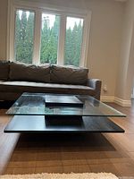 Front view showing the glass top, black wooden base, and surrounding furniture for scale.