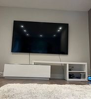 Full view of the two-piece white media table under wall-mounted TV with bottom drawer and top horizontal shelf.