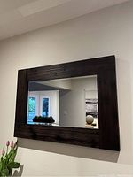 Front view of rectangular mirror with dark stained wood frame, hung on wall reflecting room details.