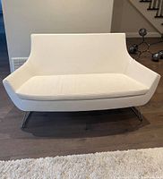 Front view of white 2-seater sofa with slim metal legs on wood floor.