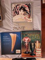 Three hardcover art books laid flat. Titles: Chinese Paintings, Studio Ceramics in Canada, Standard Encyclopedia of Carnival Glass 8th Edition. Price stickers visible indicating page count.