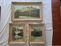 Top down view of three framed hand coloured photos showing natural mountain scenes, largest is Mt. Eisenhouer, two smaller are Moraine Lake and Three Sisters.