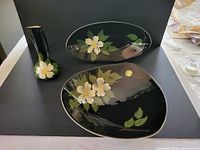 Three Herta pottery pieces on black background, including oval dish with dogwood design, unusual shaped dish, and handled vessel