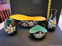 Four pieces of Herta pottery displayed from the front showing black glaze with raised dogwood flower decorations and color interiors.