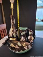 Full view of the four pieces including the lamp, two vases, and one dish with hand decorated Northern Lights design on black glaze.