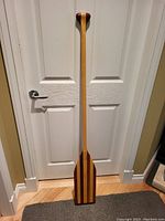 Full view of the 56 inch canoe paddle standing against a door showing the T-grip handle, straight shaft, and blade.