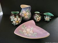Front view of all five Herta pottery pieces with floral dogwood design, showing colors and hand decoration.