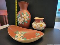 Front view of tallest 11" vase, 5.5" vase, and 11" long dish showing brown glaze and hand-painted white dogwood flowers and green leaves.
