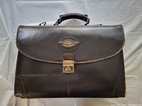 Front view of Bugatti leather briefcase showing flap with metal clasp lock and Bugatti logo plaque