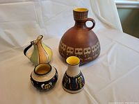 Four German art pottery pieces arranged on white fabric including largest bulbous bottle with handle, multicolored pitcher, and two smaller vases