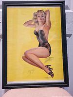 Front view of the framed vintage pin-up print showing the entire artwork of a woman in black swimsuit on yellow background.
