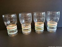 Set of four clear vintage glasses against black background showing colored bands near base.