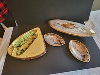 4 piece gold glazed oval shaped covered ceramic dish and 2 matching ashtrays with an additional gold glazed ashtray, all showing speckled glaze finish and mid-century style