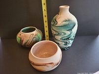 Three swirl glazed pottery pieces: one tall vase, two bowls with marbled glaze finish