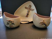 Three pieces of Herta pottery displayed on dark surface, front view showing hand-painted West Coast Indian design motifs on each piece.