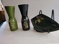Three pieces are shown together: green and black glazed vases with Raven designs and a black glazed ashtray with Thunderbird design.