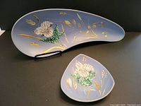 Front view of the two pottery pieces showing hand-painted pink trillium flowers on blue background with gold accents