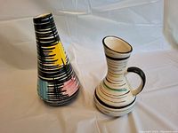 Two West German art pottery pieces, a conical decorated vase and a striped jug with handle, photographed on white background.