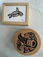 Top view of a rectangular wooden box with orca motif and a round wooden box with bird motif on lid.