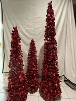 Front view of three red collapsible Christmas trees in 3ft, 4ft, and 5ft heights displayed against white backdrop.
