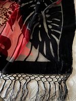 Close-up of black and red velvet-like shawl with fringed edges and floral poppy design